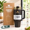 A black Stanley FlowState 40 oz tumbler with a gold logo and handle, standing beside its brown Stanley box on a marble countertop, with a softly blurred indoor background.